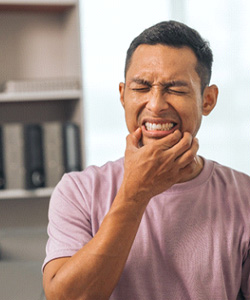 Man in pink shirt squinting and touching corners of mouth in pain
