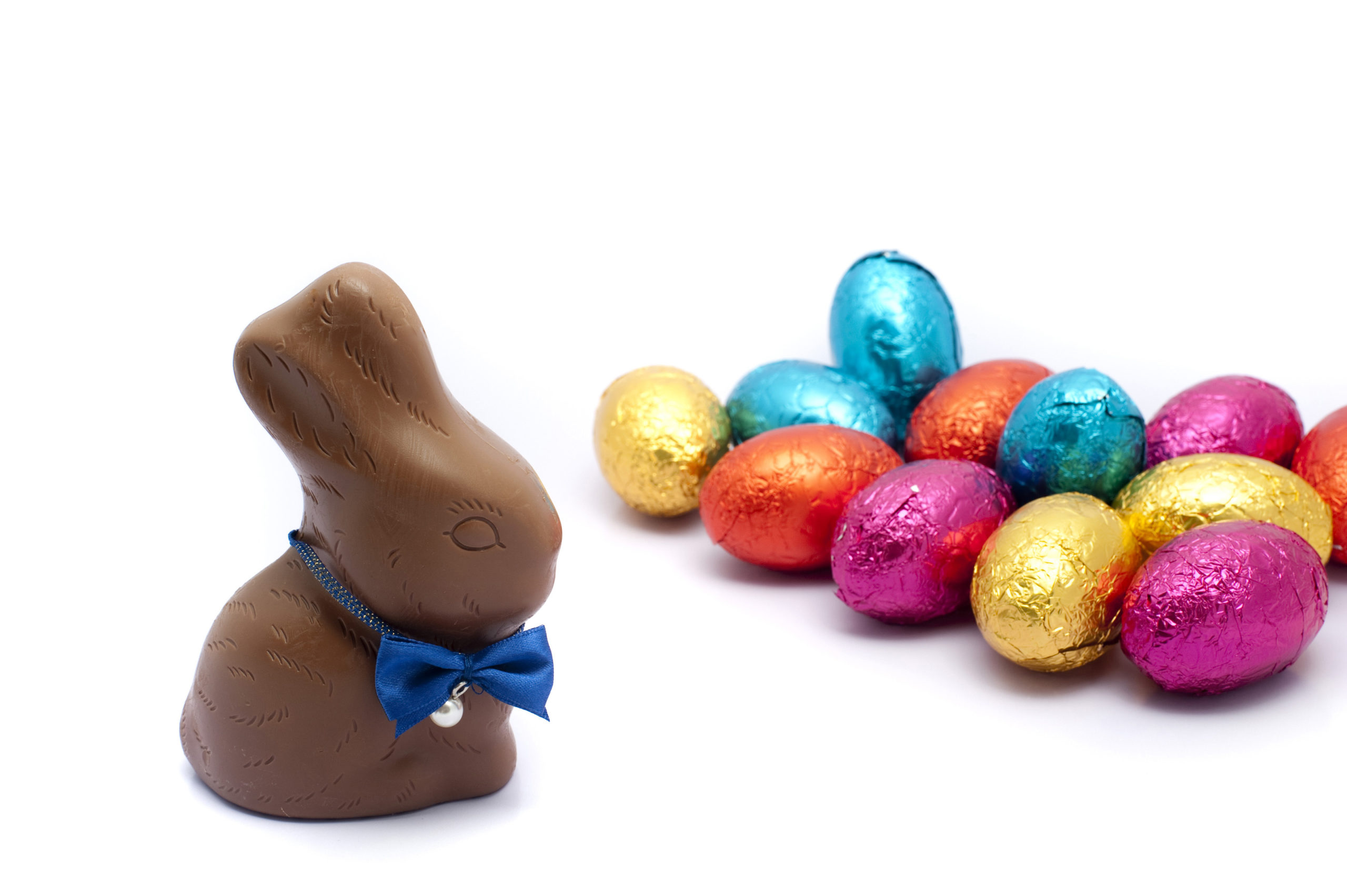Chocolate Easter egg assortment with a cute little bunny with a bowtie in the foreground with numerous colorful foil wrapped eggs behind.