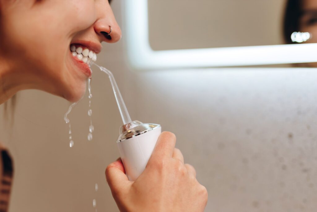 Profile view of woman flossing teeth with oral irrigator